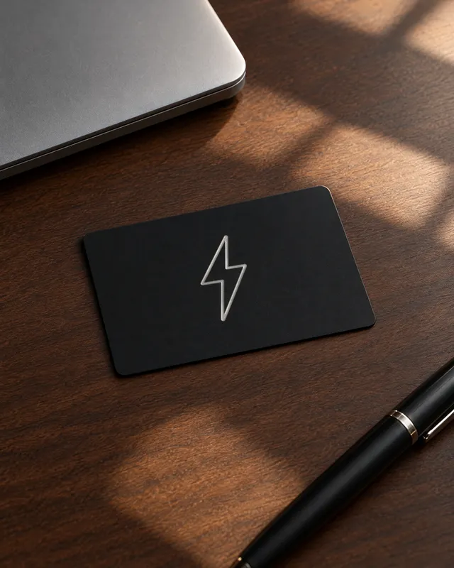 The matte black ZapCard with its silver foil bolt on a walnut desk beside a laptop and a pen
