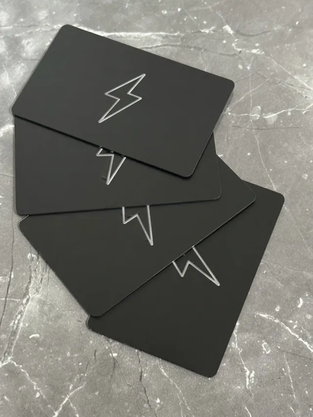 Four matte black ZapCards with silver foil bolts fanned out on marble